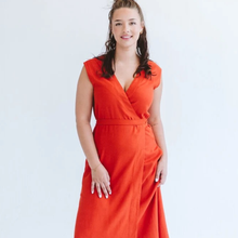 Load image into Gallery viewer, A woman wearing a sleeveless wrap-style maxi dress in a vibrant orange-red color, standing against a plain white studio background.