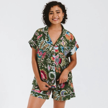 Load image into Gallery viewer, A woman modeling a dark green short-sleeve pajama set with a colorful tropical floral print and white piping, set against a plain white background.