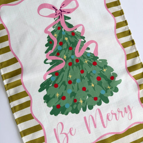 Decorative towel with Christmas tree design, pink ribbon, and 'Be Merry' text on a white background.