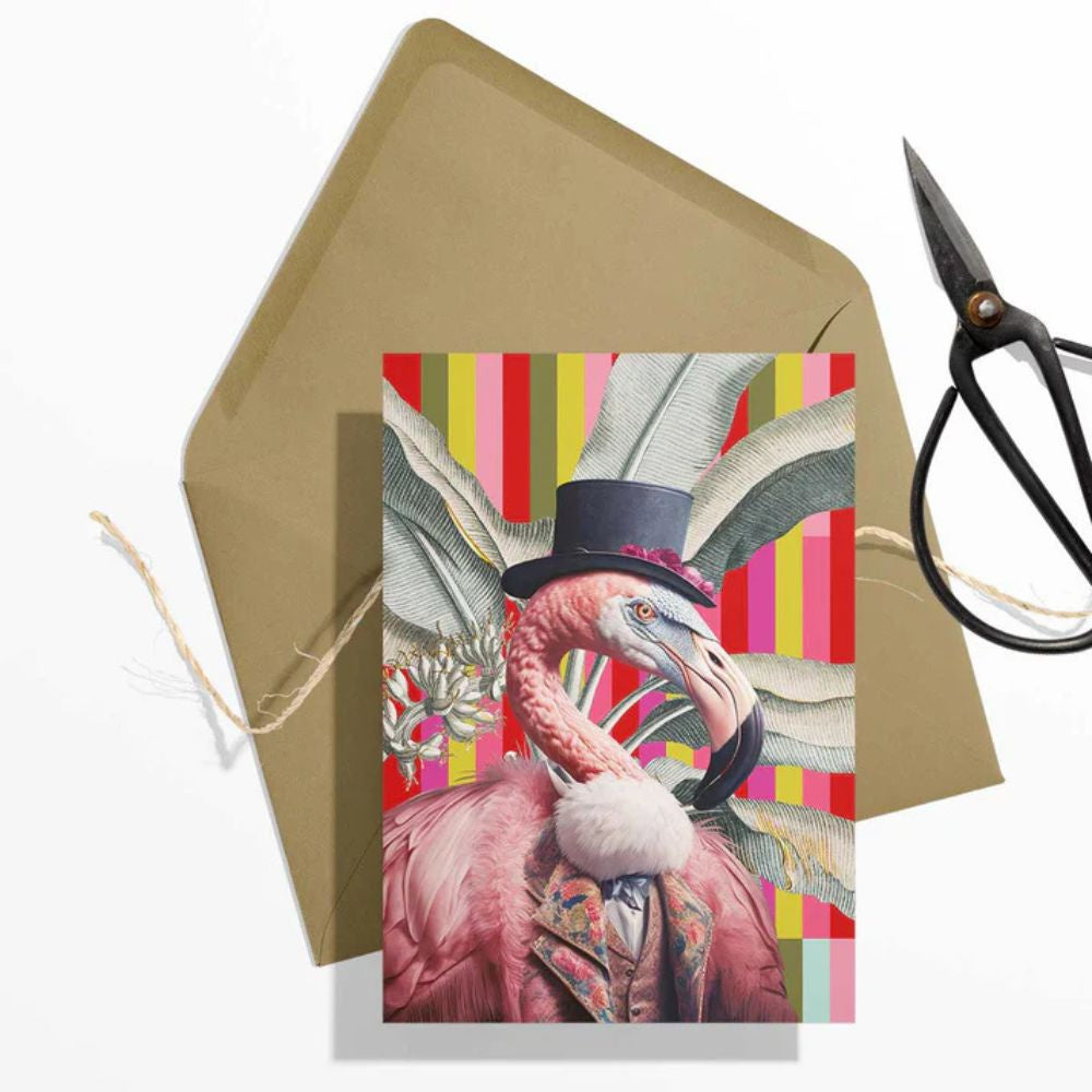 Greeting card with a flamingo wearing a top hat on a colorful striped background, with a brown envelope and scissors in the background.