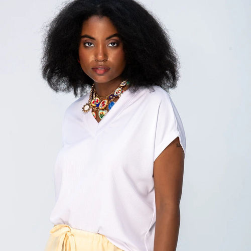 Woman wearing a white top and yellow skirt with a colorful necklace against a light gray background