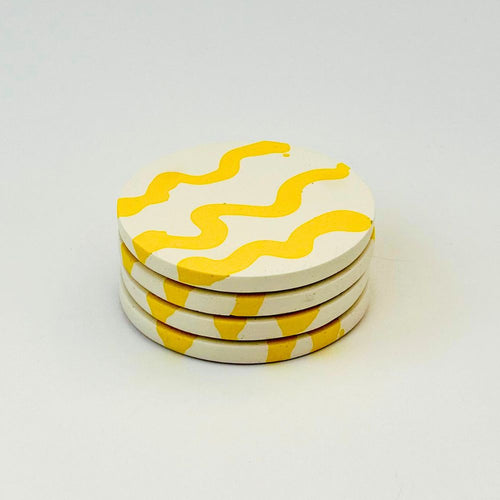 Four round coasters with yellow wavy pattern on a white background