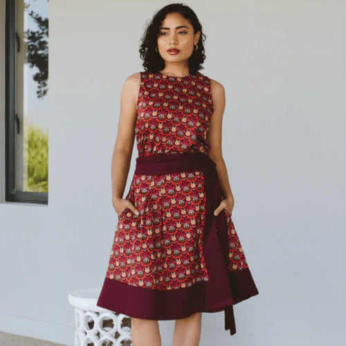 Woman wearing a red and brown patterned dress standing against a light background
