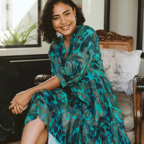 Woman in a green camo patterned dress sitting on a chair in a home setting