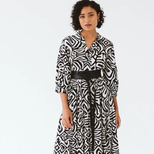 Woman wearing a black and white patterned dress with a belt on a light gray background
