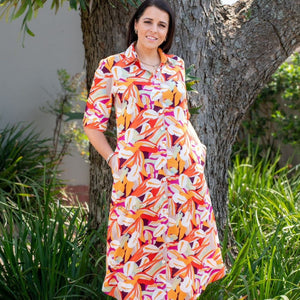 Woman wearing a colorful floral dress standing outdoors near a tree