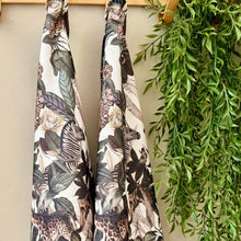 Load image into Gallery viewer, JW Designs White African safari print tea towels featuring zebras &amp; giraffes hanging on a rack next to a green plant.
