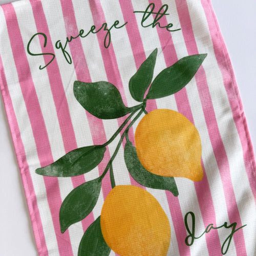 Tea towel with pink and white stripes, lemons, and leaves on a white background