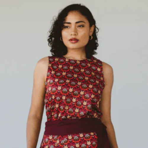 Woman wearing a sleeveless top with a red and black pattern against a plain background
