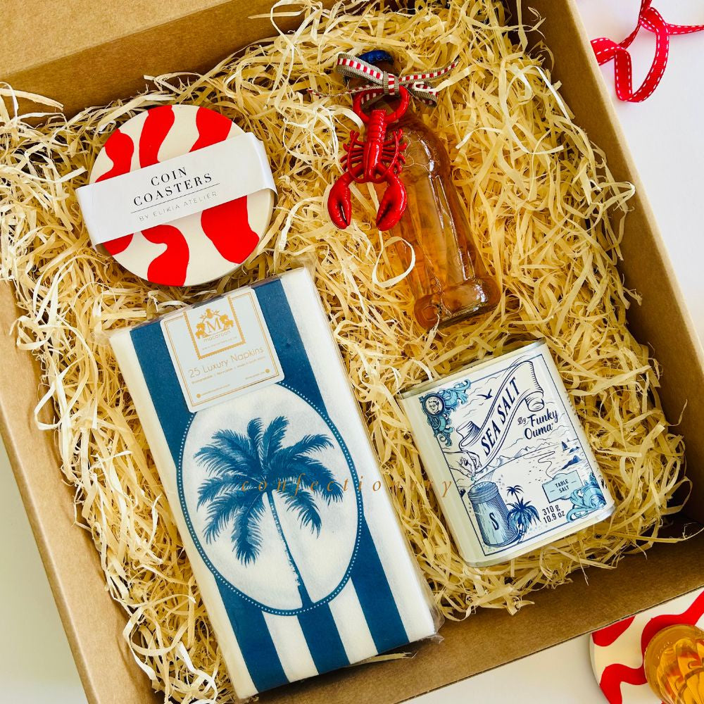 Gift box with assorted items including a set of red & white coin coasters, lobster bottle opener, paper napkins, and tin of sea salt.