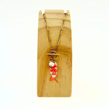 Load image into Gallery viewer, Gold necklace with an orange and white fish pendant on a wooden stand.
