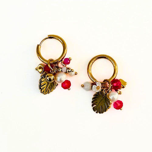 Pair of gold hoop earrings with brass leaf and red bead charms on a white background