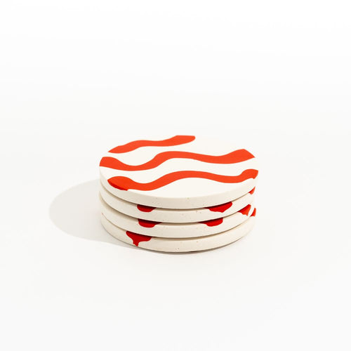 Stack of four ceramic coasters with red wavy patterns on a white background