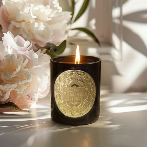 Candle in a black glass with a gold decorative label in front of flowers
