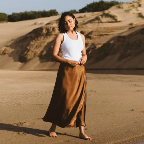Woman in a white tank top and brown skirt standing on sand dunes