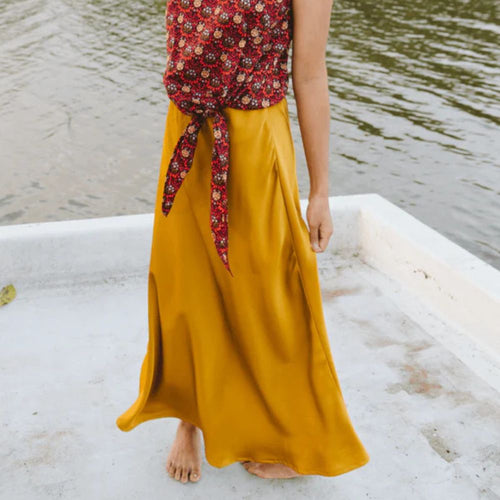 Person wearing a mustard yellow skirt and red floral top standing on a boat with water in the background