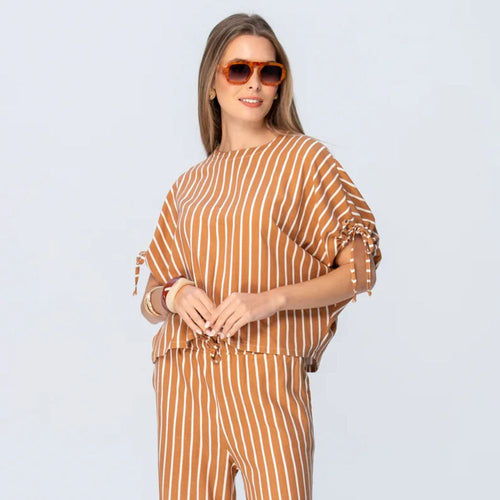 Woman wearing a brown and white striped outfit with sunglasses on a light gray background