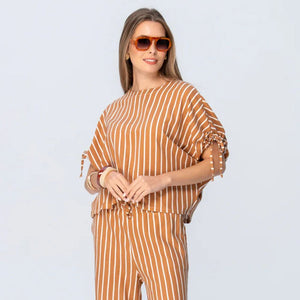Woman wearing a brown and white striped outfit with sunglasses on a light gray background