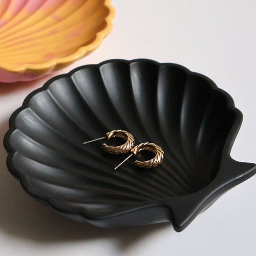 Gold hoop earrings on a black shell-shaped dish with a pink shell in the background.