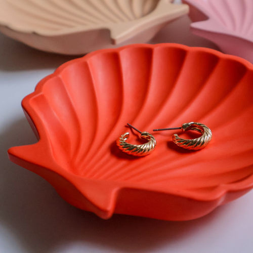 Gold hoop earrings on a red shell-shaped dish with a pink and beige background