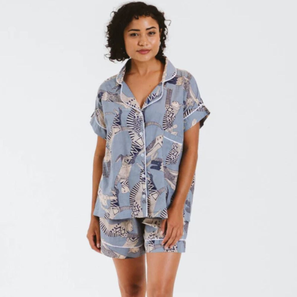 Woman wearing a matching shirt and shorts pyjama set with a blue and white pattern on a plain background