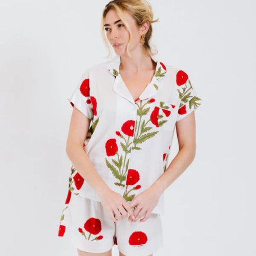Woman wearing a white pyjamas with red floral patterns on a plain background