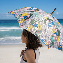 Load image into Gallery viewer, Person holding a colorful umbrella with a tropical pattern on a beach.
