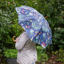 Load image into Gallery viewer, Person holding a colorful umbrella with a floral pattern in front of a green bush.
