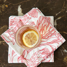 Load image into Gallery viewer, Cocktail with lemon slice on red &amp; white floral-patterned paper napkins on a marble surface
