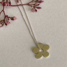 Load image into Gallery viewer, Gold flower-shaped pendant on a silver chain with pink flowers in the background
