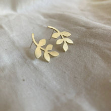 Load image into Gallery viewer, Gold leaf-shaped earrings on a beige fabric background
