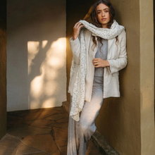 Load image into Gallery viewer, Woman wearing a light-colored outfit with a scarf against a textured wall.
