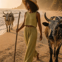 Load image into Gallery viewer, Woman in yellow outfit walking on a beach with two cows
