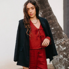 Load image into Gallery viewer, Woman wearing a red outfit with a black coat standing against a tree.
