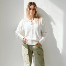 Load image into Gallery viewer, Woman wearing a white sweater and light green cargo pants against a white wall.
