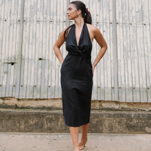 Load image into Gallery viewer, Woman wearing a black halter neck dress standing against a rustic metal wall.
