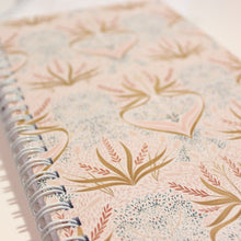 Load image into Gallery viewer, Notebook with floral pattern and spiral binding on a light background

