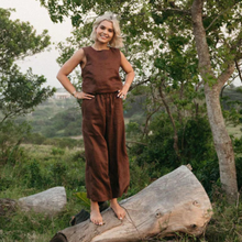 Load image into Gallery viewer, Woman in brown sleeveless top and wide-leg pants standing on a log with a natural landscape in the background
