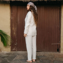 Load image into Gallery viewer, Woman in a light-colored outfit standing in front of a wooden door.
