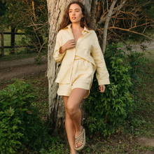 Load image into Gallery viewer, Woman in a light yellow outfit standing next to a tree in a natural setting
