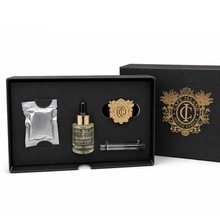 Load image into Gallery viewer, Cape Island Clifton Beach car diffuser gift set featuring a small bottle of oil with a dropper, a silver foil packet, a gold crest pin, and a glass rod, presented in an open black box with the branded lid behind it.
