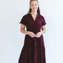 Load image into Gallery viewer, A woman wearing a short-sleeve tiered maxi dress in deep burgundy, standing against a plain white background.
