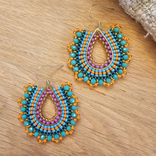 Load image into Gallery viewer, A pair of handmade beaded teardrop dangle earrings with turquoise, orange, purple, and black beads, displayed on a light wood surface.
