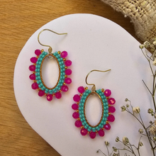 Load image into Gallery viewer, A pair of handmade bohemian-style dangle earrings with turquoise and magenta beads, displayed on a white ceramic dish over a wooden surface.
