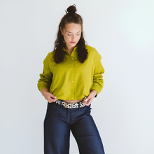 Load image into Gallery viewer, Woman wearing a bright green shirt and blue jeans against a white background
