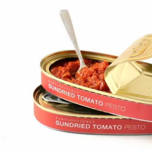 Open can of sundried tomato pesto with a spoon inside, on a white background