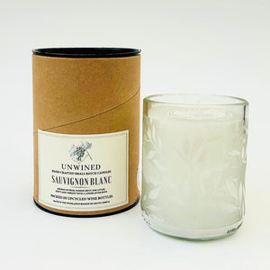 Candle in a glass container with a cardboard tube labeled 'Unwined Sauvignon Blanc' on a white background