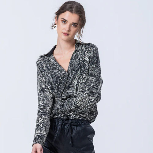Woman wearing a black and white patterned blouse against a light gray background